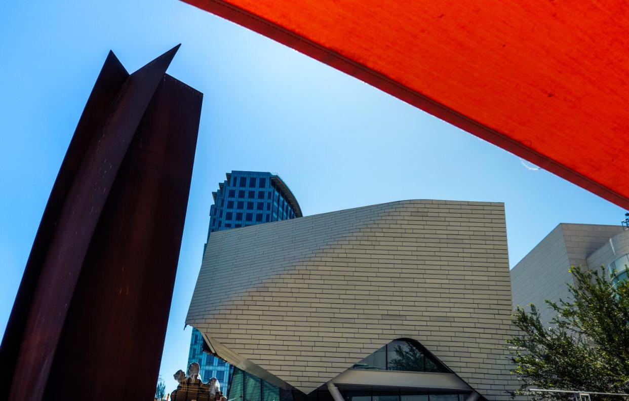 A tall, pentagonal steel sculpture stands beside two buildings.