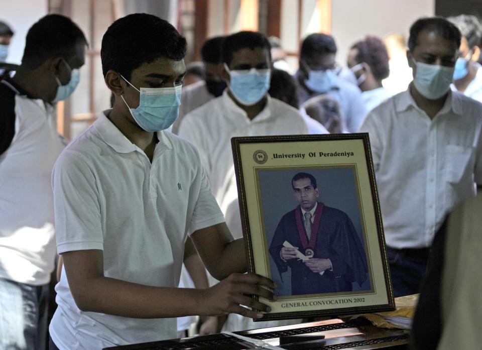 Gavith, a son of Sri Lankan factory manager Priyantha Kumara who was lynched by a Muslim mob in Pakistan for alleged blasphemy places a portrait of his father on the casket during the burial in Colombo, Sri Lanka, Wednesday, Dec. 8, 2021. (AP Photo/Eranga Jayawardena)