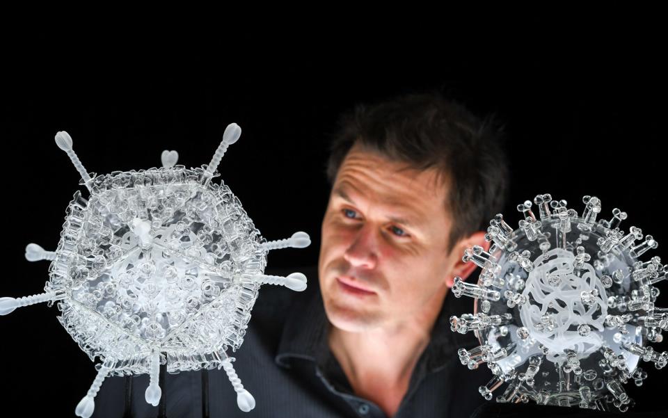 Artist Luke Jerram with his glass sculpture of the Oxford-AstraZeneca coronavirus vaccine, left, alongside his earlier work of the virus itself, in glass at the Paintworks in Bristol  - Finnbarr Webster/Getty Images