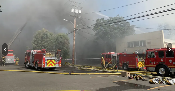 Four fire trucks sit amid thick smoke on a city street.