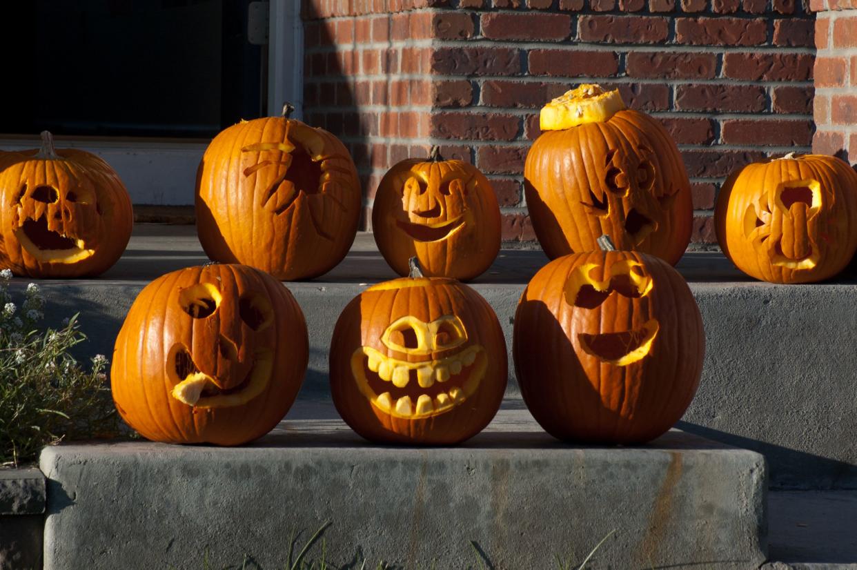 Eight cute carved pumpkins on a door stoop.