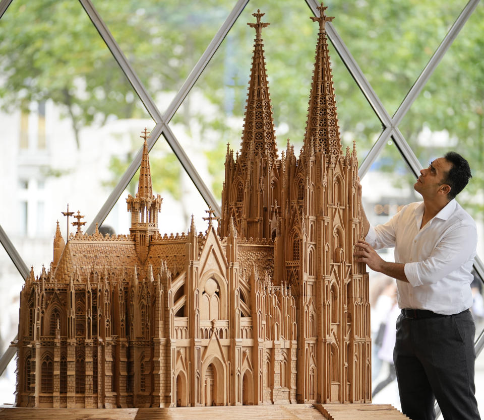Fadel Alkhudr from Syria poses beside his wooden model of the word heritage Cologne Cathedral on display at the Domforum in Cologne, Germany, Monday, June 20, 2022. Fadel Alkhudr, 42, a woodcarver and artist orginally from Aleppo, Syria, fled the war in his home country and arrived in the western german city of Cologne in 2015. In 2019 he started to carve the local Cologne Cathedral in his small basement - without any plans or drawings, using only cell phone photos of the cathedral as a template. (AP Photo/Martin Meissner)