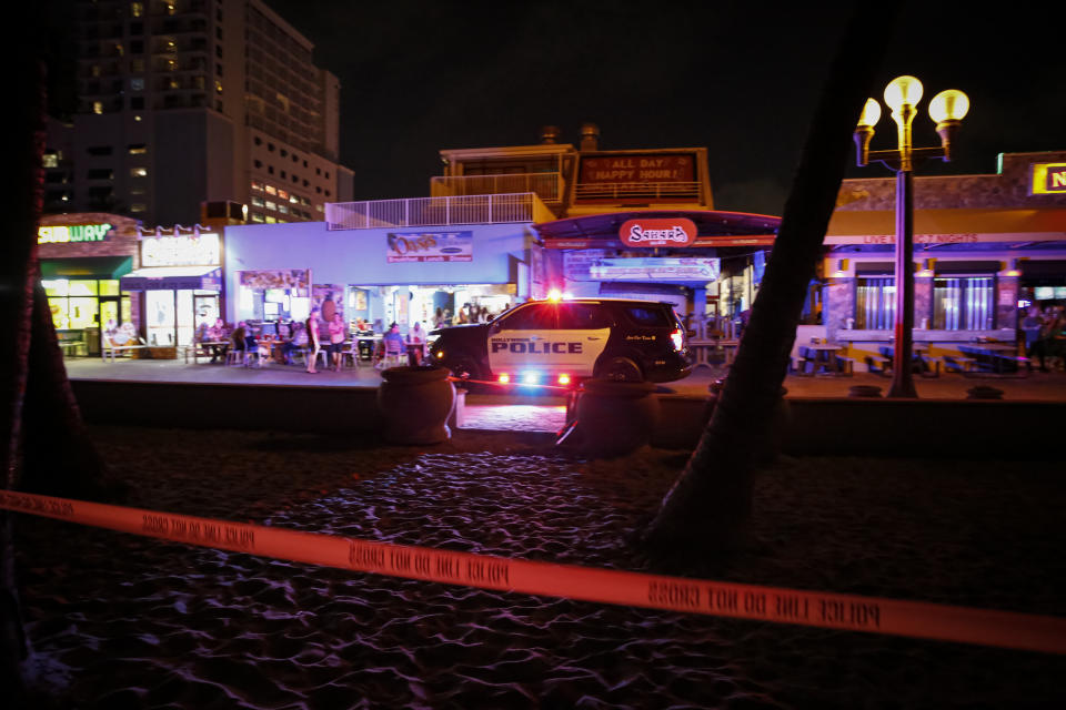 Police cordon off the scene of a mass shooting in Hollywood, Florida. Palm trees and sand can be seen in the foreground.