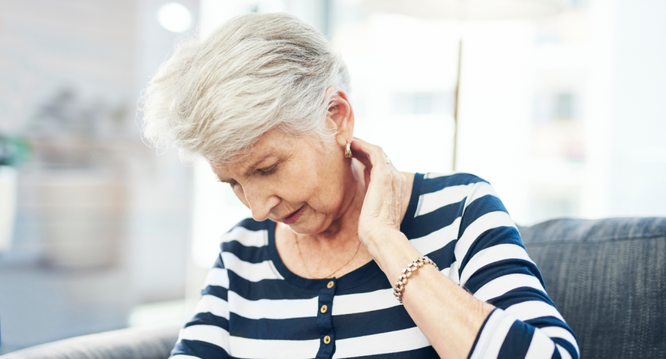 old woman in striped shirt holding neck in pain