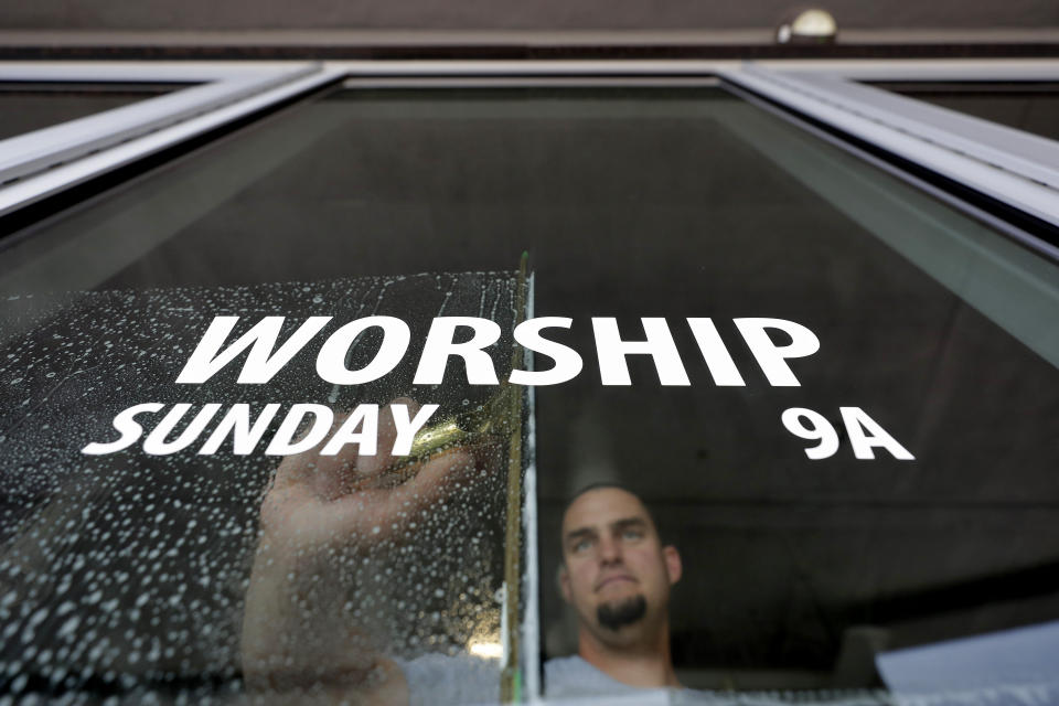 Grace Bible Church facilities manager Kenny Sitton sanitizes entry door glass at the church Friday, March 13, 2020, in Tempe, Ariz. after church leaders participated in a state-wide conference call with Arizona Disease Control that highlighted the state's guidelines for preventing the spread of COVID-19 coronavirus in houses of worship. The church stated that morning Services are currently scheduled to continue with the exceptions of canceled child care, reconfigured seating to promote social distancing and gloved-greeters who will open and close doors for service attenders. (AP Photo/Matt York)