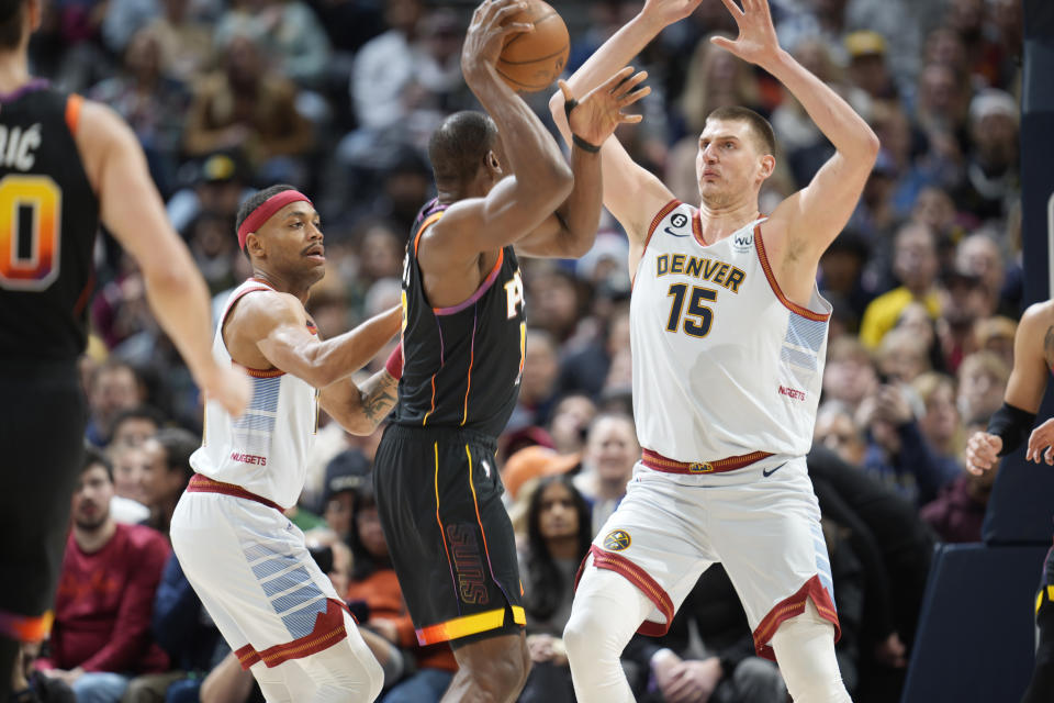 Phoenix Suns center Bismack Biyombo, middle, looks to pass the ball as Denver Nuggets forward Bruce Brown, left, and center Nikola Jokic defend in the first half of an NBA basketball game Wednesday, Jan. 11, 2023, in Denver. (AP Photo/David Zalubowski)