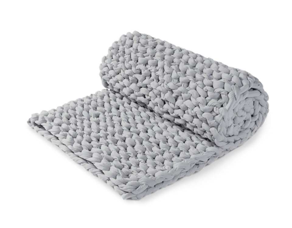 A grey heavily knotted rolled up Hand Woven Weighted Blanket against a plain background.