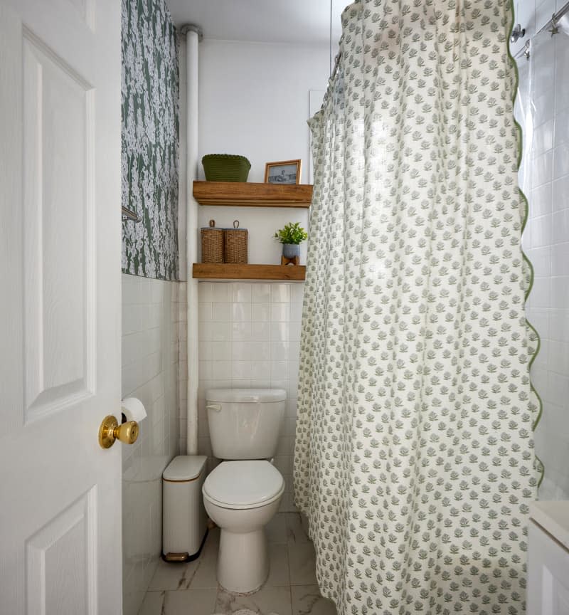 Wood shelves hung above toilet in bathroom with green and white shower curtain.