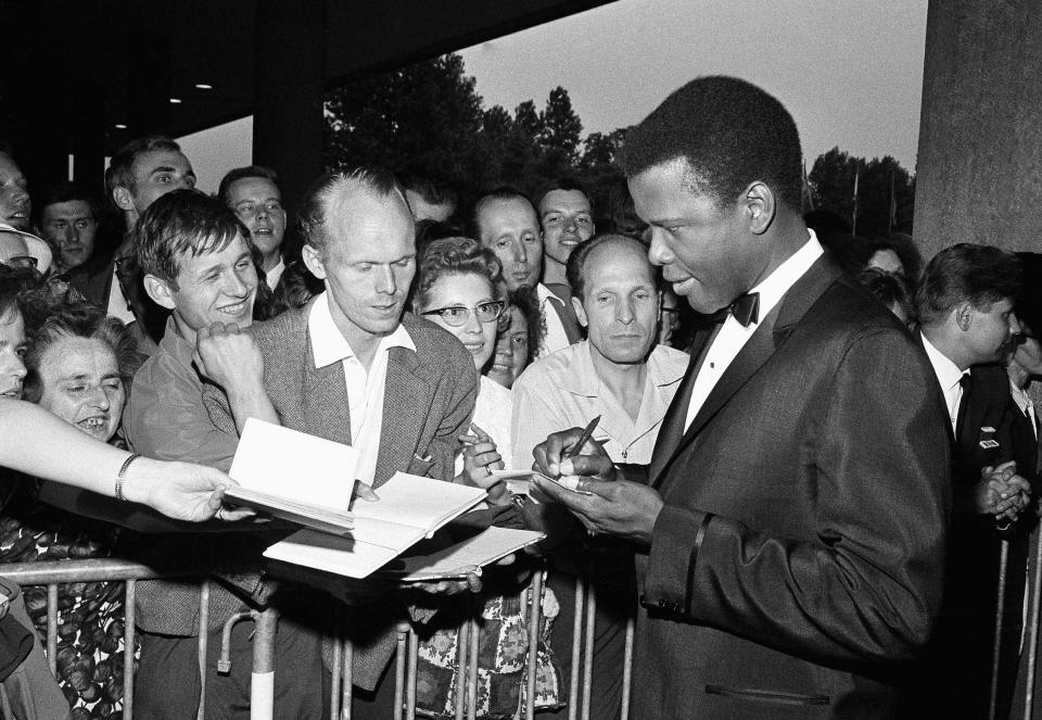 ARCHIVO - Sidney Poitier firma autógrafos antes de la inauguración del 14o Festival Internacional de Cine en la sala de convenciones de Berlín Occidental el 26 de junio de 1964 en Berlín. Poitier, el actor pionero e inspiración que transformó la manera en la que era retratada la gente negra en pantalla y se convirtió en el primer actor negro en ganar un Premio de la Academia en un papel protagónico y el primero en ser una potencia de la taquilla murió el jueves 6 de enero de 2022 en Bahamas. Tenía 94 años. (Foto AP/Edwin Reichert, archivo)
