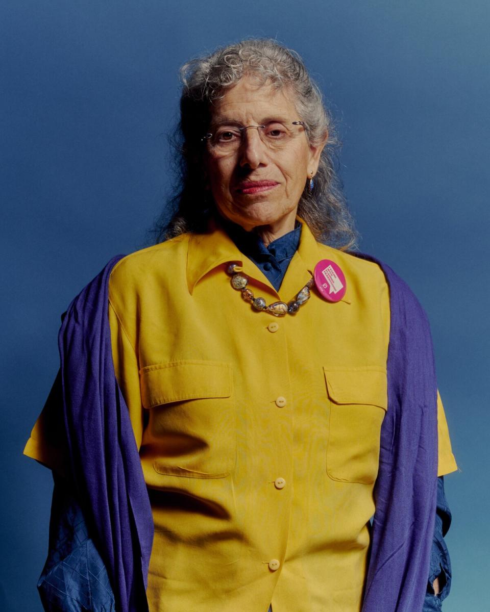 A woman in a yellow shirt stands against a blue background.