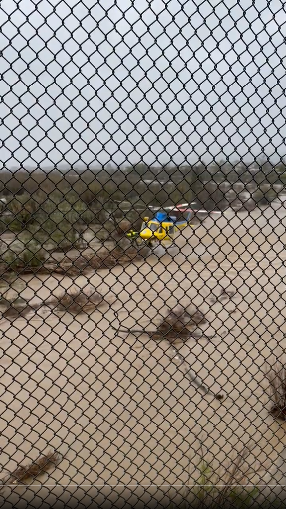 A Ventura County helicopter crew member in yellow jacket can be seen beckoning to one of three people stranded on an island in the Santa Clara River in Fillmore on Wednesday.