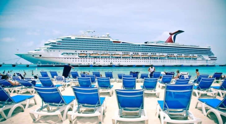 Carnival (CCL) cruise ship on water in front of beach with chairs