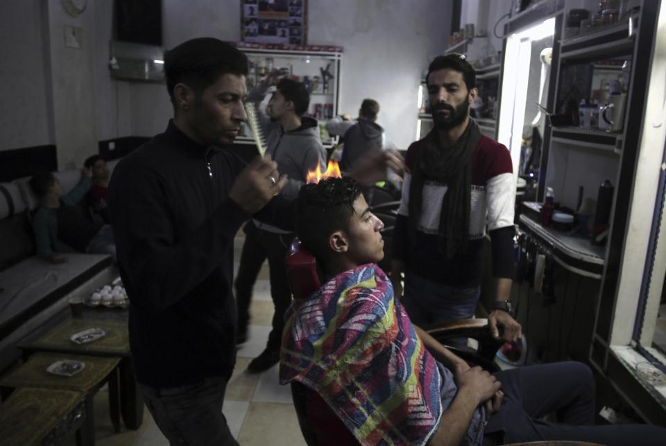 In this Wednesday, March 15, 2017 photo, Palestinian hair dresser Ramadan Adwan uses fire to straighten the hair of a costumer in his barber shop in Rafah refugee camp in the Gaza Strip. After cutting and combing, the barber applies what he calls "special" lotion and powder client's heads to protect their skin before using an aerosol can to burn hair off. (AP Photo/ Khalil Hamra)