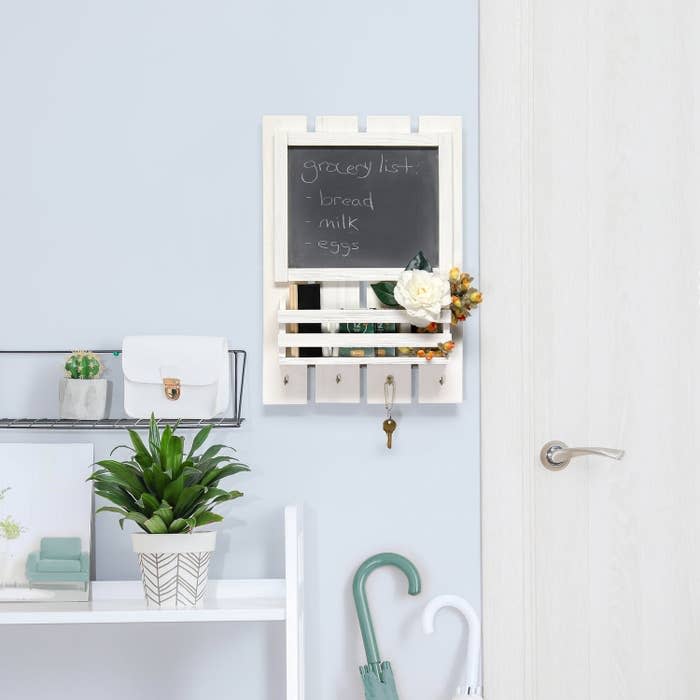 Wall-mounted organizer with a blackboard listing "bread, milk, eggs," a white wallet, plant, and umbrella stored below, in a neatly arranged entryway setup