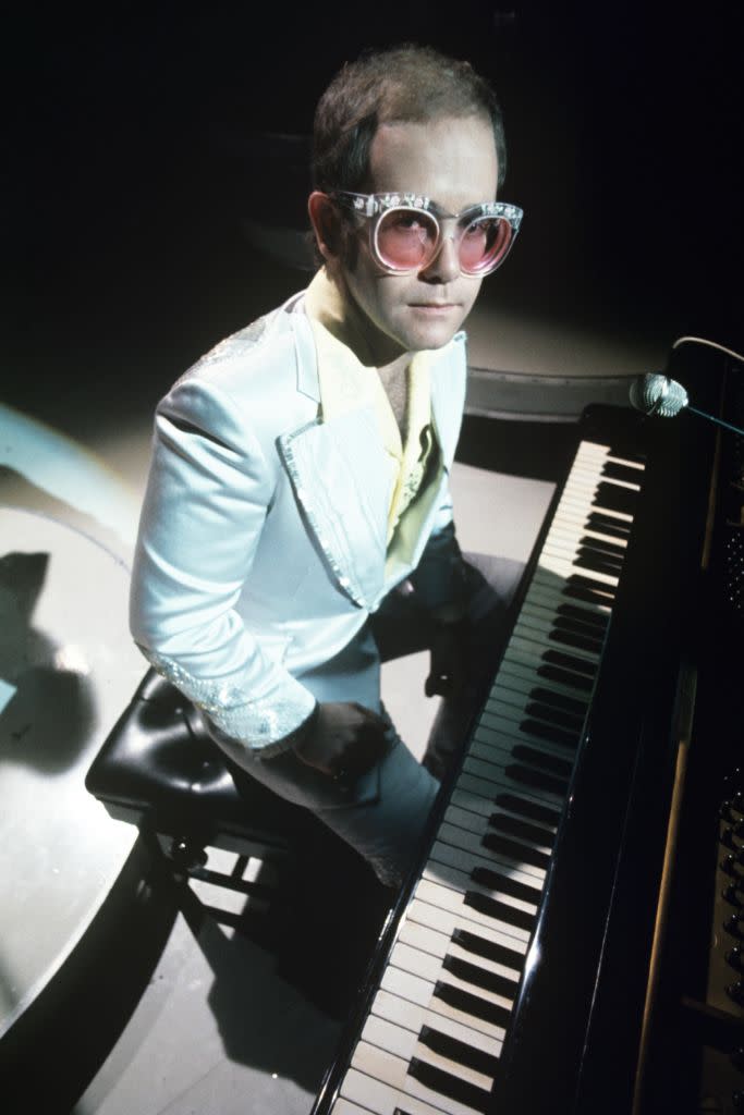 Elton John performing on “The Russell Harty Show” in 1974. The singer had some of the most flamboyant performance looks of the decade, donning sky-high platforms with his equally ostentatious sparkly sunglasses. - Credit: Shutterstock