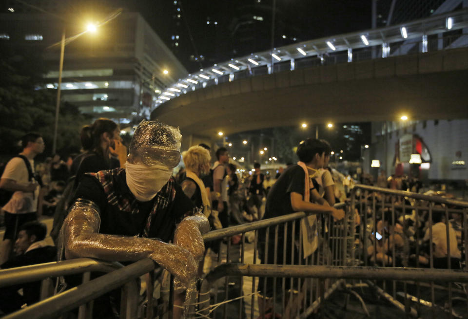 Wrapped in plastic to shield from pepper spray, a student protester stands behind a makeshift barrier blocking main streets in the central business district of Hong Kong, late Monday, Sept. 29, 2014.  (AP Photo/Vincent Yu)