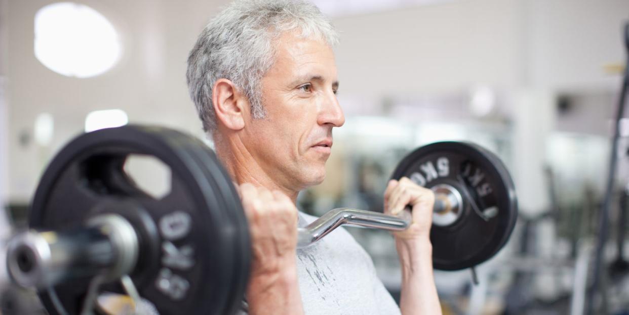 portrait of smiling man holding barbell in gymnasium