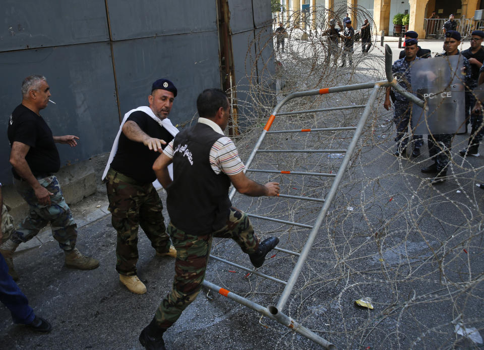 Lebanese retired soldiers, step on the barbed wires, as they try to enter the parliament building where lawmakers and ministers are discussing the draft 2019 state budget, in Beirut, Lebanon, Friday, July 19, 2019. Lebanese protesters rallying against an austerity budget have broken through a security cordon outside the parliament where lawmakers were voting on the controversial draft bill. (AP Photo/Hussein Malla)
