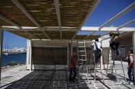 Workers install a bamboo screen at a bar restaurant in Chora, on the Aegean island of Naxos, Greece, Tuesday, May 11, 2021. Greece Friday became the latest country to open up its vacation season as it dismantles lockdown restrictions and focuses its vaccination program on the islands. (AP Photo/Thanassis Stavrakis)