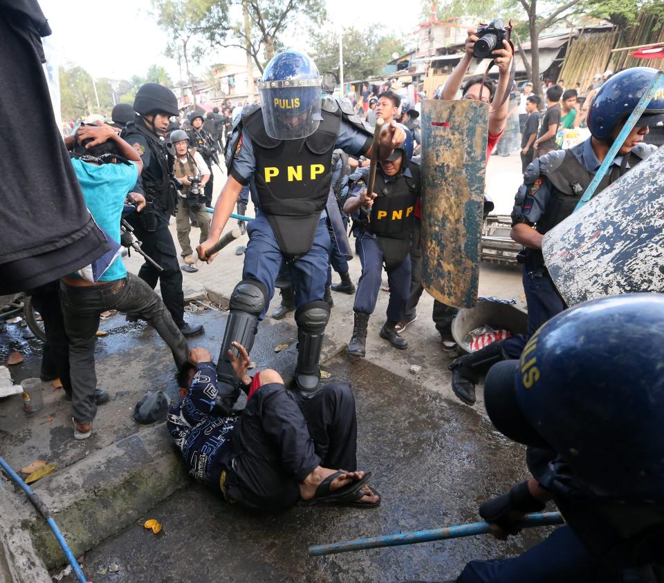 epa04044224 Filipino policemen kick an informal settler during a demolition of shanties at Sitio San Roque in Quezon City, east of Manila, Philippines, 27 January 2014. Throwing rocks, pillboxes, and even human waste, illegal settlers barricaded the demolition team in Baranggay Bagong Pag-asa. Four residents were arrested and twelve were reported injured. Residents report receiving cash from 300 to 450 US dollar in exchange for their voluntary relocation. Earlier, hundreds of the urban poor marched to the city hall in protest of the demolition that will pave the way for the rise of a business district. EPA/DENNIS M. SABANGAN