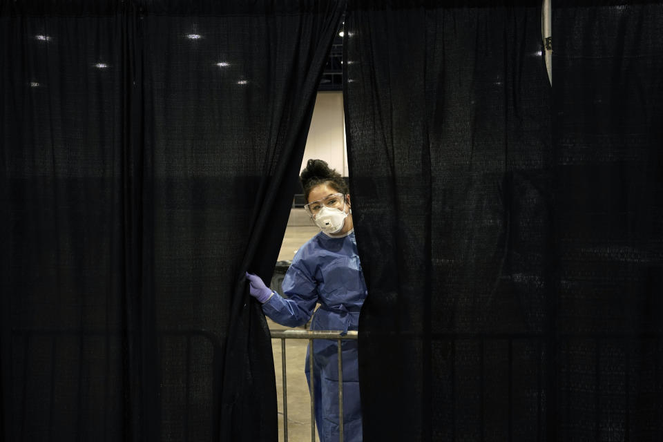 Diana Vega, a registered respiratory therapist, peeks through a curtain during setup at a temporary coronavirus testing site Monday, Aug. 3, 2020, in Las Vegas. (AP Photo/John Locher)