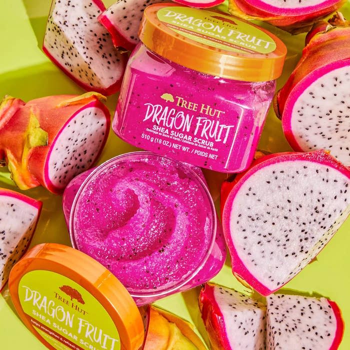The open container, showing the hot pink scrub's texture, surrounded by dragon fruit slices on a yellow background