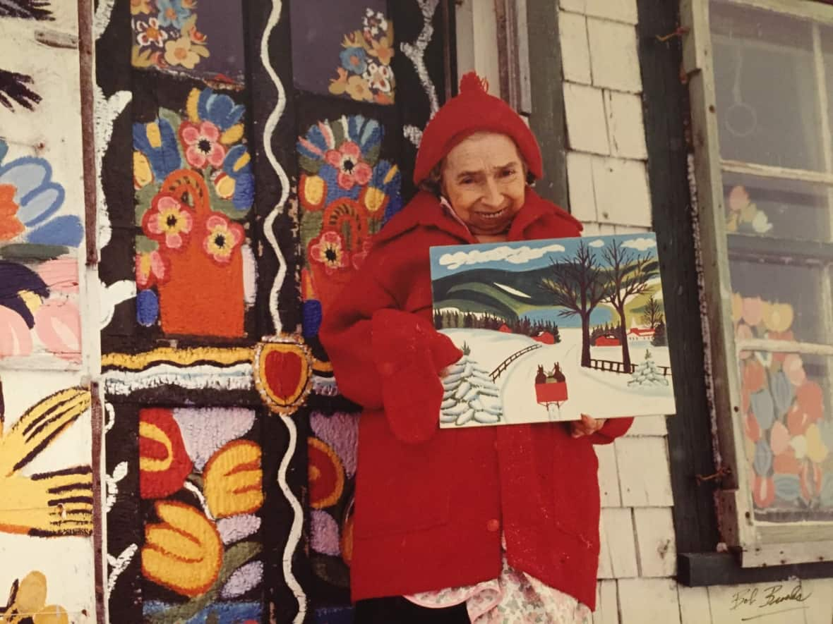 Maud Lewis poses in front of her home with one of her paintings. Frauds of the late Nova Scotian folk artist's work date back decades. (Bob Brooks/Art Gallery of Nova Scotia - image credit)