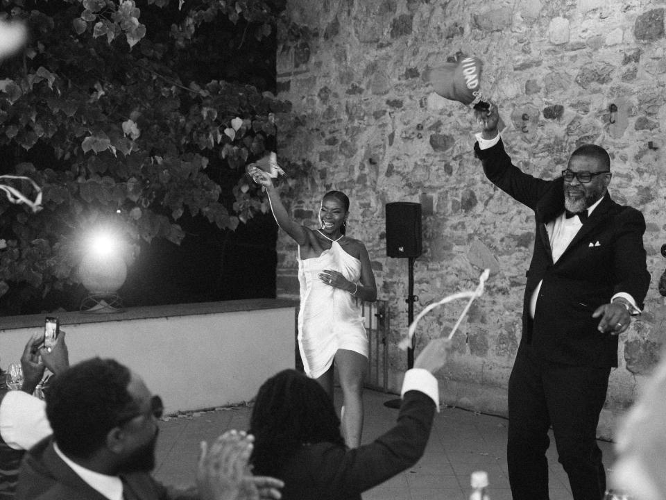 A bride and her father throw hats in a black-and-white photo of them dancing.