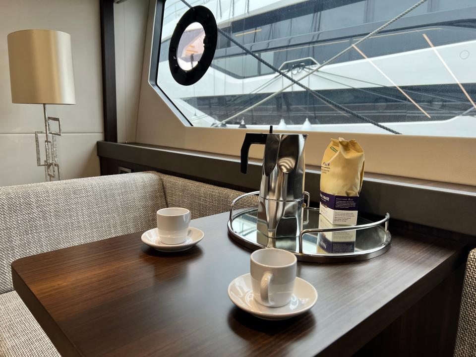 A cafetiere and bag of ground coffee and two espresso cups on the dark wood table in master cabin of Sunseeker 76
