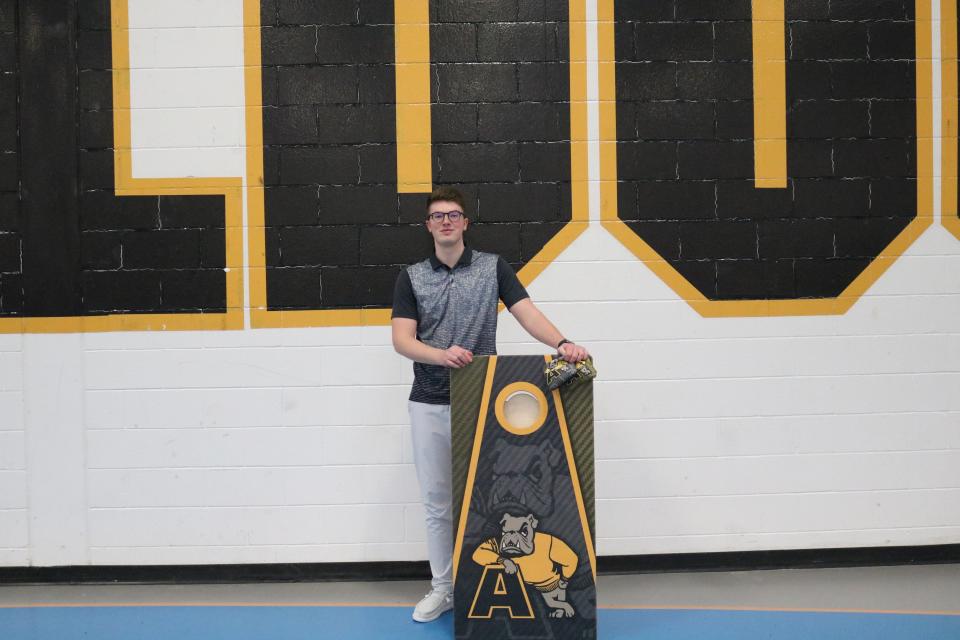 Adrian College cornhole coach Max Benedict (Tecumseh) stands with a pair of cornhole bags and a cornhole board emblazoned with the Adrian colors on Monday, Feb. 14 at the Merillat Sport and Fitness Center.
