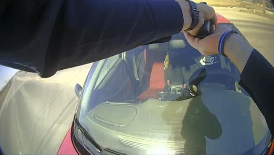 In this image taken from police body cam video and released by the Carroll County Attorney, Carroll, Iowa, police Officer Patrick McCarty points his pistol at Dennis James Guider Jr. as Guider flees with McCarty on the hood of a car after a traffic stop on March 5, 2021, in Carroll, Iowa. Guider kept driving as McCarty clung to the vehicle, screaming at him to put on the brakes. Eventually McCarty was thrown from the vehicle, breaking his back. Guider, 29, from the Chicago area, was sentenced last week to up to five years in prison after pleading guilty to a felony count of serious injury by vehicle. (Carroll County Attorney via AP)