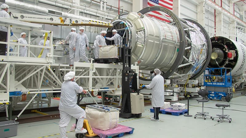  Scientists are seen in their clean room clothes with a giant metal cylinder representing the new experiment. 