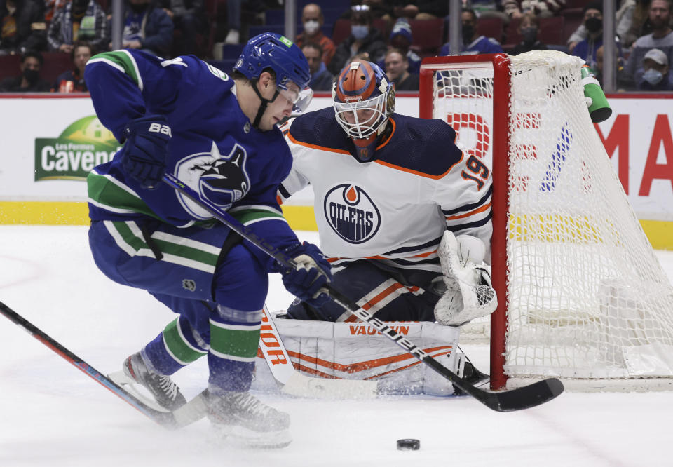 Vancouver Canucks' Nils Hoglander, left, of Sweden, skates with the puck around the back of the net behind Edmonton Oilers goalie Mikko Koskinen, of Finland, during the second period of an NHL hockey game, Tuesday, Jan. 25, 2022 in Vancouver, British Columbia. (Darryl Dyck/The Canadian Press via AP)