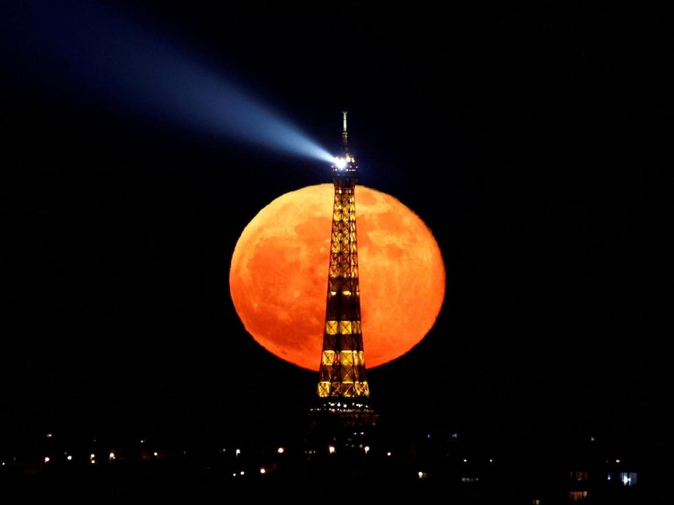 An orange-looking full moon rises behind the eiffel tower