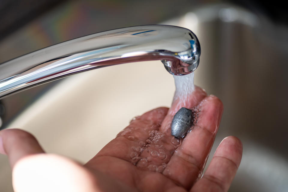 Person holding lead metal in water flow from tap. Lead is harmful to humans and exposure to the metal can affect 'multiple body systems.' (Getty)