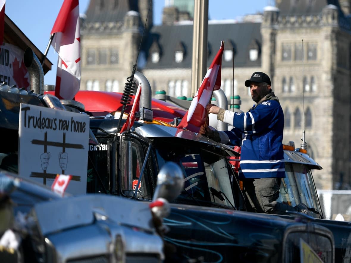 A protester affixes a flag to the top of their truck, parked beside a truck with a sign calling for the jailing of Prime Minister Justin Trudeau, outside Parliament Hill, as a protest against COVID-19 restrictions ontinues into its second week in Ottawa on Monday, Feb. 7, 2022. (Justin Tang/The Canadian Press - image credit)