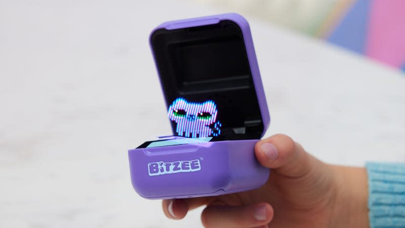 A user holding the Bitzee digital pet with the lid open and a purple kitten on the display.