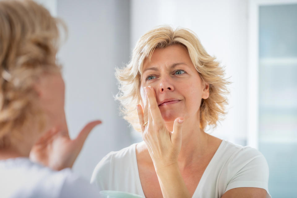 Mature woman looking at skin in mirror, flaxseed benefits for skin