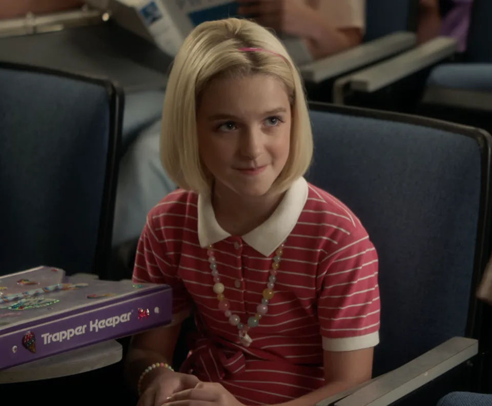 Paige in a striped polo and beaded necklace, sitting in class