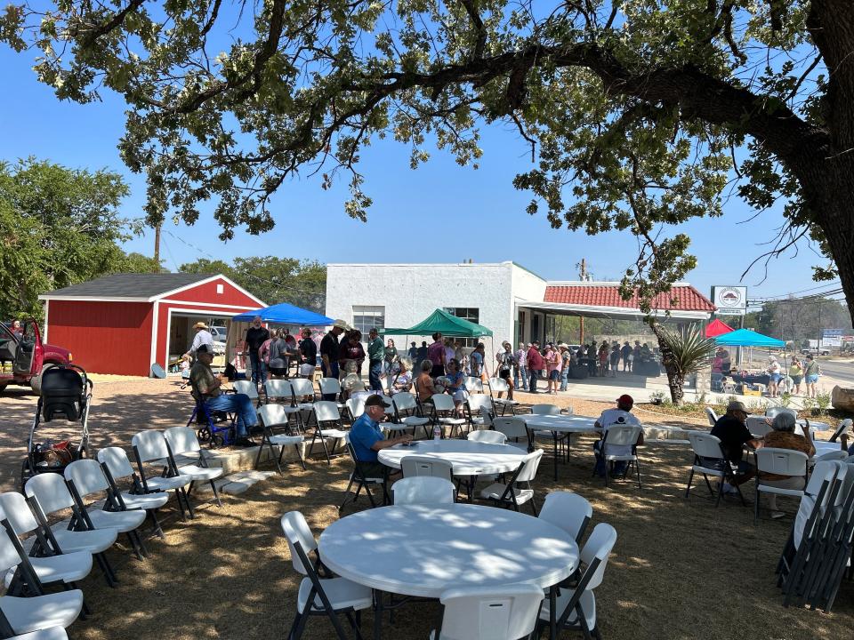 A crowd of people surround white tables and a renovated gas station at the opening of Menard Station, a farmer's market in Menard, Texas.