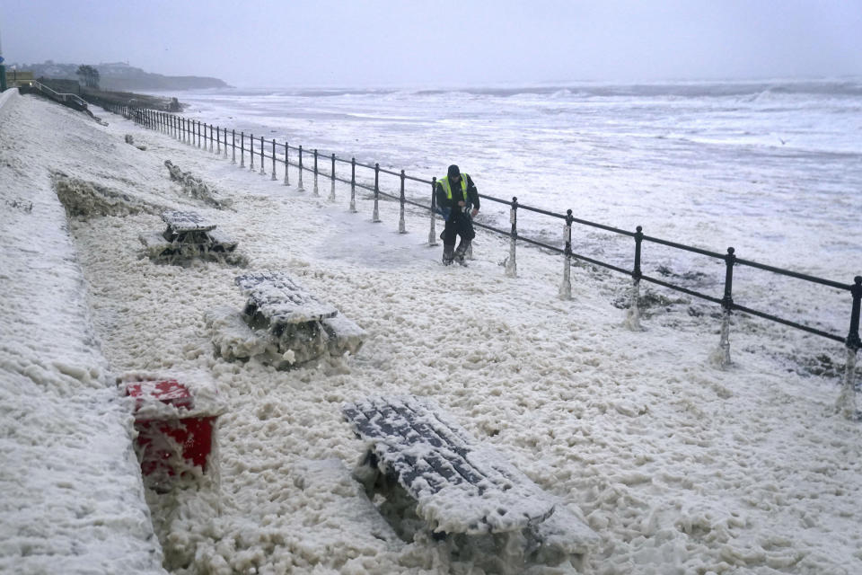 A man walks through sea foam in Seaburn, northeastern England, Friday, Oct. 20, 2023. The gale-force winds are expected to hit hardest the eastern part of Denmark's Jutland peninsula and the Danish islands in the Baltic Sea. But the British Isles, southern Sweden, northern Germany and parts of Norway also on the path of the storm, named Babet by U.K.’s weather forecaster, the Met Office. (Owen Humphreys/PA via AP)