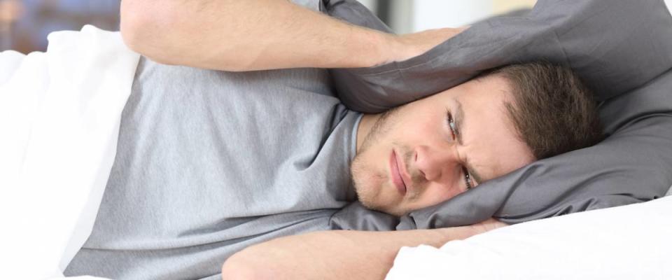 One man trying to sleep covering ears to avoid neighbor noise at home