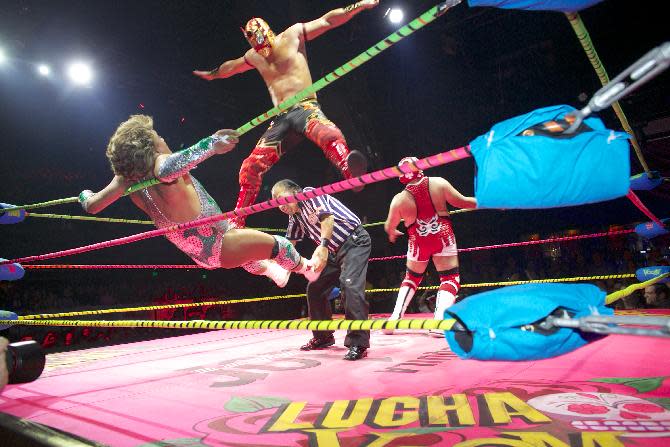 In this Wednesday, Feb. 12, 2014 photo, wrestler Niebla Roja, top, flies over referee Platainitos, to land on wrestler Cassandro, left, during a performance at Lucha VaVoom's Valentine’s show at The Mayan Theatre downtown Los Angeles. At right, wrestler, Dr. Maldad. The esoteric hybrid of American burlesque and Mexican wrestling is an outrageous hit. (AP Photo/Damian Dovarganes)