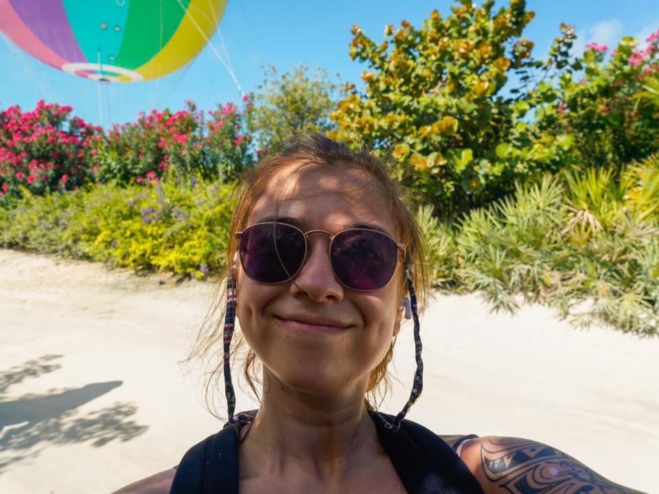 The author takes a selfie with sunglasses on at CocoCay with sand, plants, and a hot air balloon in the background