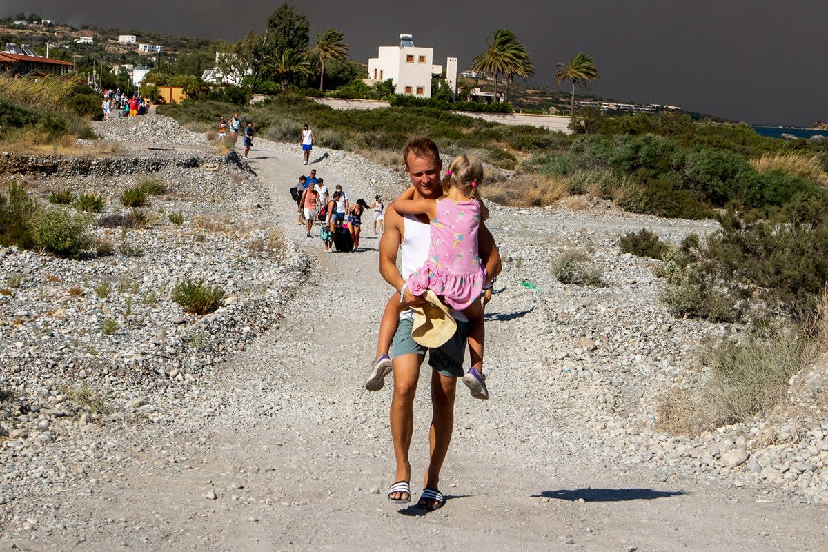 A man carries a child as they leave an area where a forest fire burns on the island of Rhodes (AP)