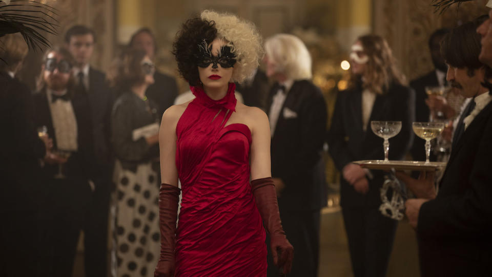 Cruella (Emma Stone) walks through a party in a red dress and mask.