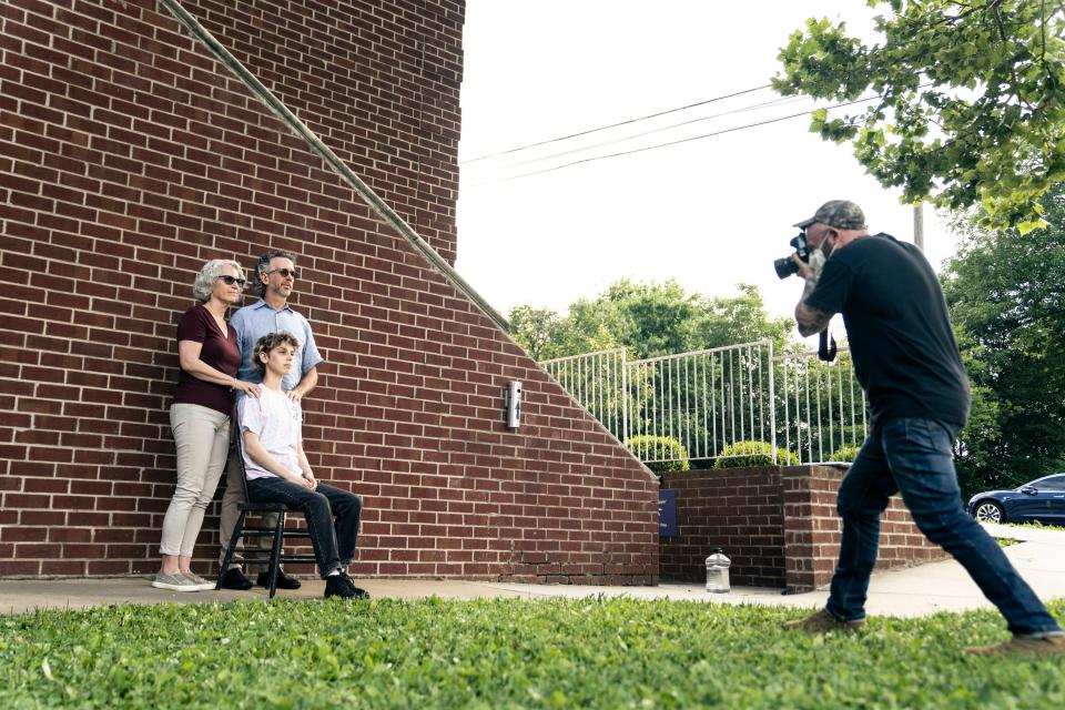 Jesse Freidin taking a portrait of a family in front of a brick wall on a bright day.