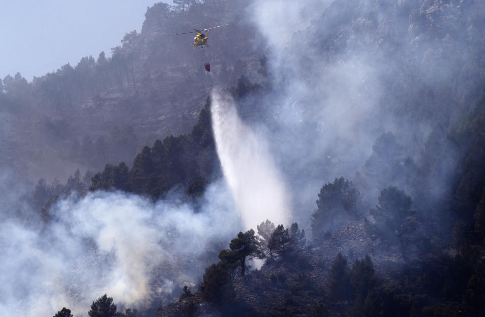 A helicopter drops water to extinguish a forest fire in Montanejos, Castellon de la Plana, Spain, March 26, 2023. A prolonged drought after a record-hot 2022 appears to have brought the wildfire season forward and Spanish officials are now bracing for more huge fires. (AP Photo/Alberto Saiz)