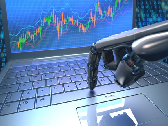 A robotic hand using a laptop to trade, with a rising stock chart on the laptop's monitor.