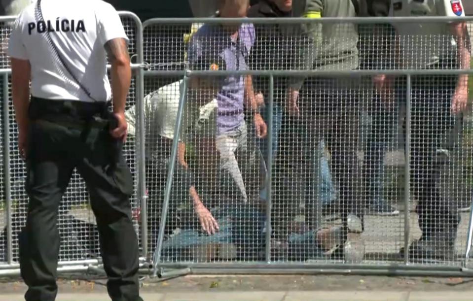 A man lies on the ground with security guards above him.